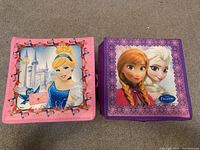 Front view of the two fabric storage boxes, one pink with Cinderella, the other purple with Anna and Elsa from Frozen.