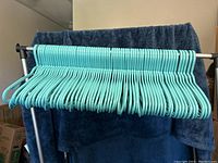 Front view of light turquoise plastic clothes hangers placed on a metal rack with a blue towel background