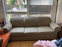 Fabric upholstered beige sofa from front showing three seat cushions and rolled arms.