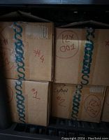 Four cardboard boxes stacked with handwritten labels such as #4 and #1, containing bulk makeup.