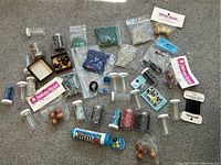 Overview photo showing multiple seed bead containers, packets, and loose beads arranged on carpet.