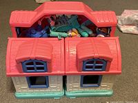 Closed dollhouse with visible red roof and packed dolls and furniture inside.