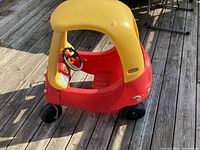 Red and yellow Little Tikes Cozy Coupe toddler car, viewed from the side, showing overall condition with a small seat crack visible.