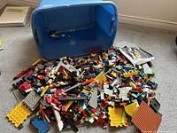 Bin of assorted Mega Blocks pieces including various plates and bricks spilled on the floor next to a blue plastic bin.
