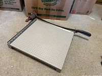 Large paper cutter with grid cutting surface and handle located on floor.