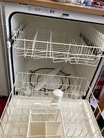 View of the dishwasher interior with one rack and white plastic rinse aid dispenser in bottom center.