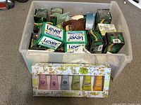 Large clear plastic container full of multiple Lever 2000 soap bars and other soap bars in packaging, plus a boxed set of Crabtree & Evelyn lotions in front