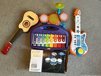 Overview of all toy musical instruments including two guitars, a xylophone, a small orange drum set, and two boxed desktop drum sets