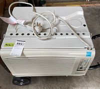 Front view of NOMA window air conditioner on hand cart showing grille, plug, and top surface with handle.