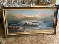 Full view of framed seascape painting showing ocean waves, rocks, sky, and signature.