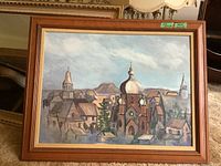Frontal image of framed painting showing the church with onion dome and surrounding village, cloudy sky above.
