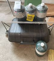 Four Coleman propane tanks on top of a portable grill with closed lid and handle.
