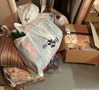 Photo showing various items including striped chair cushions, plastic bags filled with linens or pillows, and a cardboard box.