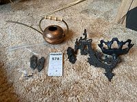 Copper watering can, cast iron wall sconce, and some hardware pieces displayed on carpet.