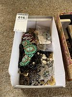 Box of assorted costume jewelry including necklaces and pendants with different colors and designs, mostly worn condition