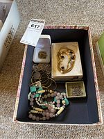 Box containing various necklaces, chains, and three jewelry boxes, displayed on carpeted floor.