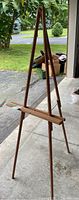 Full view of the wooden art easel standing upright in a garage area with outside visible.