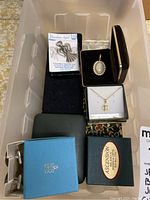 Photo of assorted religious and other costume jewelry items in boxes, including angel pin, cameo pendant, cameo brooch, and cufflinks.