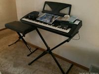 Yamaha PSR-340 keyboard setup on metal stand with music book and accessories on top, accompanied by a folding bench.