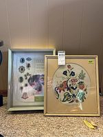 Image showing the packaged new silver shadow box frame and the framed embroidery art with floral design side by side.