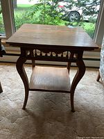 Front view of vintage Victorian solid wood table with curved legs and spindled side rail, placed indoors on carpet.