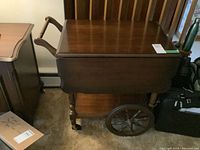 Front and side view of the wooden tea cart showing drop-leaf side, large spoked wheels, and handle.