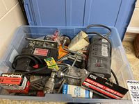 Bin filled with assorted tools, hardware, surge protector, and workshop items, showing variety of parts and devices.