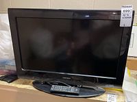Front view of the black Toshiba 26-inch TV with remote placed on the TV stand.