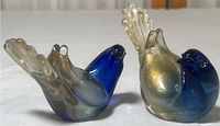 Pair of Murano glass blue and gold dove figurines shown upright on white surface.