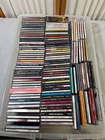Photo showing a large collection of music CDs arranged in rows on a surface. Visible titles span many artists and albums.