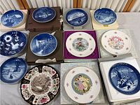 Photo showing twelve collector plates laid out on a surface, with blue and white winter and scenic themes as well as floral and character imagery.