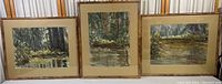 Photo showing three framed watercolor paintings with forest and pond landscapes arranged side by side.