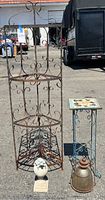Four level corner plant rack with decorative scrollwork and light surface rust, standing next to small side table with mosaic tile top and turtle statue along with glass sculpture lamp on ground.