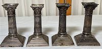 Four sterling silver candlesticks shown upright side by side displaying fluted column design and square bases with decorative edging.