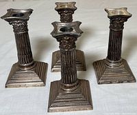 Front view of four sterling silver weighted candlesticks showing their detailed fluted and floral column design along with square bases.