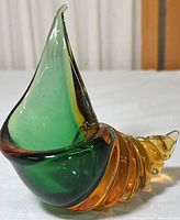 Front and side views of a vintage Murano glass conch shell showcasing green and orange tones and smooth sculpted shapes.