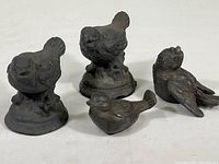 Set of four cast metal bird figurines, two with flat bases, all dark colored with detailed features.