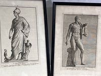 Two black-framed art prints displayed side-by-side on small stands. Left print features a robed female Roman figure labeled Minerva with an eagle and small figure beside her. Right print shows a nude male Roman figure labeled Gladiator Victor holding a statuette beside a draped pillar. Both prints contain historic style engravings and text below the images.