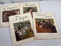 Four large books on table, each with title and artwork on cover from Impressionist painters: Cezanne, Renoir, Degas, Toulouse-Lautrec.