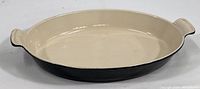 Front and side view showing oval black baking dish with cream enamel interior and handle detail.