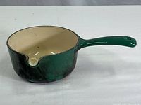Front-side view of the green Le Creuset saucepan showing the cream enamel interior and green exterior with chipping.