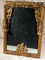 Full view of the ornate gold painted wood framed mirror with carved figures and decorations.