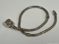 View of the silver rope style bracelet coiled on a flat surface showing its clasp and snake chain design.