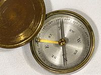 Close-up of the compass face inside the brass case, showing the directional and degree markings with the needle pointing north and east as expected.