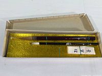 Two vintage Chinese calligraphy brushes inside a paper storage box lined with gold fabric, showing box wear.