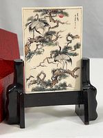 Frontal view of miniature carved plaque on black wood stand next to red display box