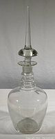 Full view of tall vintage clear glass apothecary bottle and stopper showing overall shape and size.