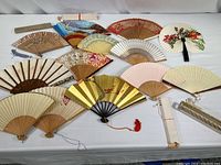 Overview photo showing all 17 vintage hand fans of various colors and designs laid out on white surface
