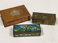 Three vintage metal boxes: one copper with crest, one brass with painted relief, one brass with enamel floral design
