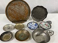 Overview photo of various metalware plates, cups, and bowls laying flat on a white surface.